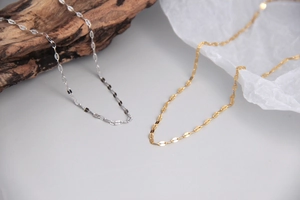 Close-up of thin minimalist S925 silver flat link chain necklaces in gold and silver