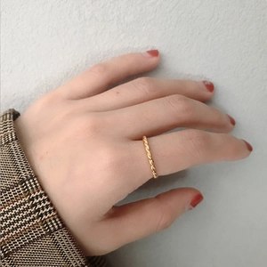 Close-up of a minimalist 18K gold rope ring on a finger showing twisted texture