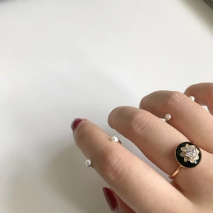 Close-up of black enamel flower ring and pearl open ring set on a hand with red nails