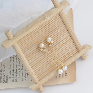 Detail view of long gold tassel earrings with pearls and crystals on wooden display stand