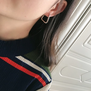 Close-up of geometric trapezoid silver earrings worn on ear with polished finish