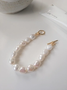 Close-up of Baroque pearl bracelet with golden toggle clasp on white surface