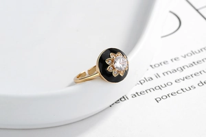 Close-up of golden floral open ring with black enamel inlay and zircon stone detailing