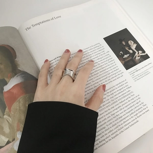 Close-up of minimalist wave-shaped silver wide ring on hand over artistic book page
