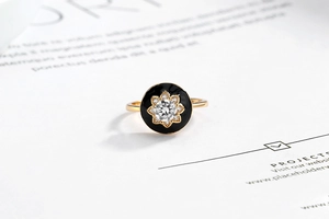 Macro shot of gold ring with black enamel floral design and sparkling center stone