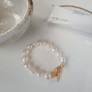 Detailed macro view of Baroque pearl bracelet with golden OT toggle clasp on white surface