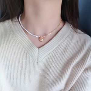 Elegant asymmetrical gold chain necklace with white pearls and a heart pendant worn on a sweater