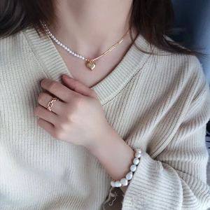 Asymmetric heart pendant necklace with pearls and gold chain on beige sweater