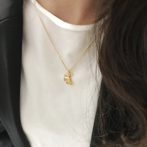 Detail of a gold pleated crescent pendant necklace worn on a neck with a black blazer
