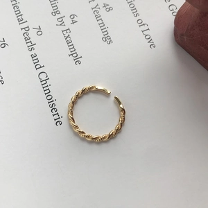 Detailed view of an adjustable golden rope twist ring on a minimalist magazine background