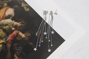 Detailed view of silver star tassel earrings with zircon inlay on art magazine background
