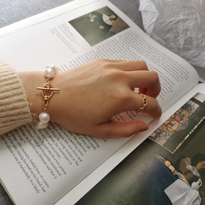 Detail of a Baroque pearl bracelet and golden anchor link ring on a classic art book