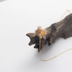 Detail of a textured golden cylindrical pendant with small crystals on a fine chain