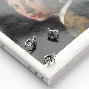 Detailed view of silver butterfly ear cuffs on an artistic book background