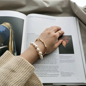 Close-up of Baroque pearl bracelet with bamboo-style gold bangle on a classic art background