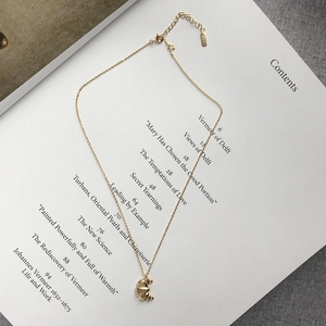 Detail of a gold pleated crescent necklace pendant on a minimalist art book background