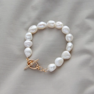 Detailed macro view of white baroque pearls with a gold OT toggle clasp on grey fabric