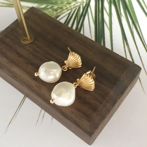 Elegant gold shell earrings with natural white baroque pearls on a wooden display block
