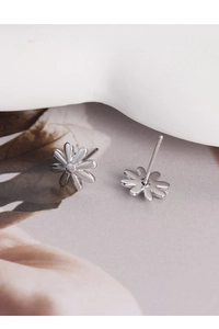 Macro shot of silver daisy stud earrings with detailed petal texture and floral background