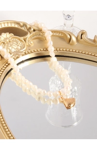 Détail macro de perles naturelles et pendentif éventail doré sur plateau miroir