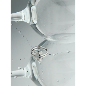Dettaglio anello infinito in argento S925 con zircone su superficie d'acqua lucida