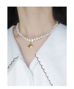 Détail d'un collier en argent S925 avec perles blanches et pendentif coquillage doré