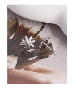 Macro shot of silver daisy stud earrings featuring detailed petals on a vintage background