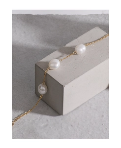 Detail of three white pearls on a minimalist gold chain against a grey concrete background
