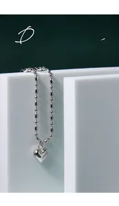Macro detail of silver heart pendant on a polished bead chain against an artistic backdrop