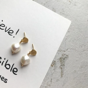 Detail of gold shell earring with baroque pearl against a minimalist white background