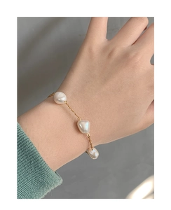 Detail of three baroque pearls on an 18K gold chain bracelet worn on the wrist
