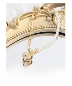 Macro view of gold heart charm and white pearl link bracelet on mirrored surface