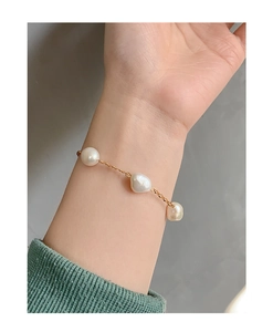 Close-up of three baroque pearls on a slim gold chain bracelet worn on a female wrist