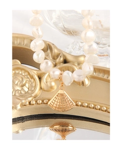 Détail d'un collier de perles baroques avec pendentif éventail doré sur un plateau miroir