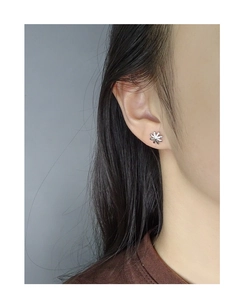 Close-up of minimalist S925 sterling silver daisy stud earrings worn on the earlobe