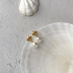 Detailed close-up of S925 silver pearl earrings with golden shell design in white dish