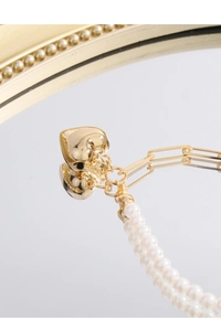 Detail of gold heart pendant with paperclip chain and white pearls on mirror