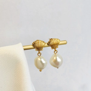 Close-up of golden shell stud earrings with elegant baroque white pearls on a metal stand