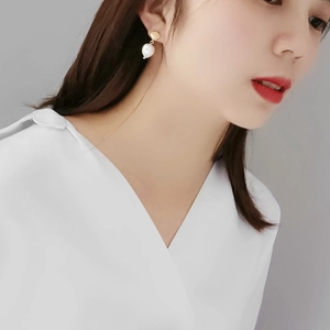 Close-up of a gold shell earring with a white baroque pearl drop worn by a model