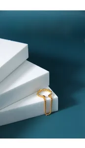 Detail of a gold chain link ring with a dangling fringe chain on white geometric blocks