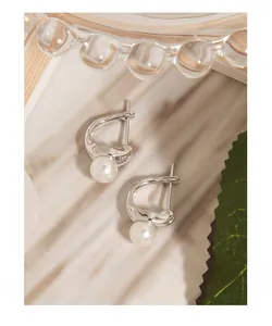 Macro detail of irregular silver streamline pearl earrings on a natural textured surface