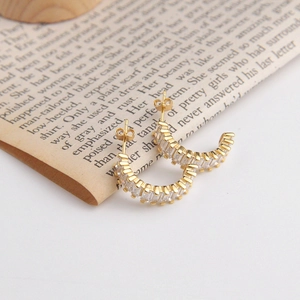 Detail of C-shaped gold earrings with channel-set baguette-cut cubic zirconia stones