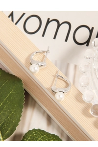Detail of silver drop earrings with white pearls on a minimalist magazine background