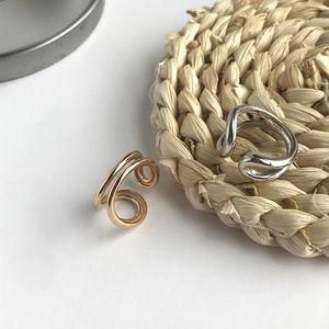 Close-up of minimalist gold and silver knot rings on a textured straw mat background