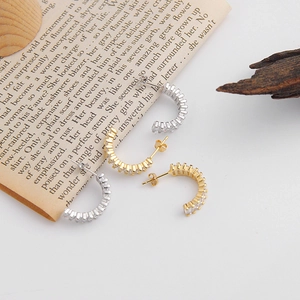 Close-up of C-shaped hoop earrings with baguette cut zircons in gold and silver finish