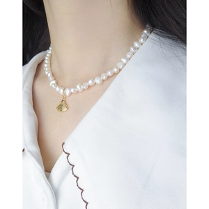 Collier de perles baroques avec pendentif coquille dorée porté sur chemise blanche