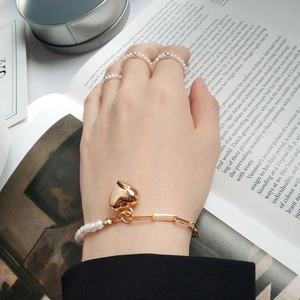 Detailed shot of an asymmetric pearl bracelet with gold heart pendant and ring set