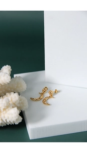 Close-up of golden crescent moon earrings with irregular hammered texture on white stand