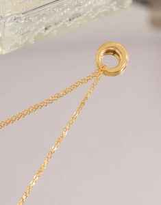 Vue détaillée d'un pendentif anneau doré sur chaîne fine avec reflets sur le miroir