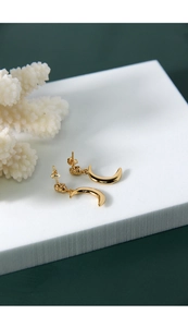 Detail of gold crescent moon earrings with irregular pleated texture on a white stand